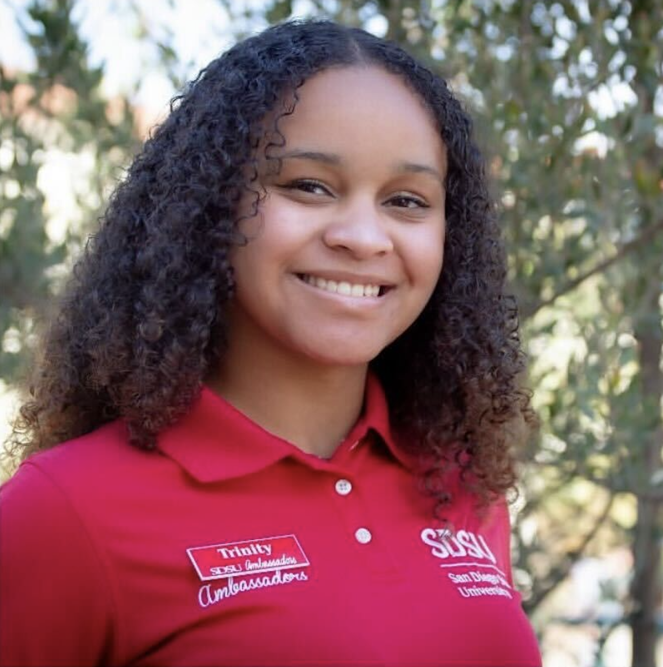 Headshot of Research Assistant Trinity Rivera wearing a red shirt and standing in front of a tree.